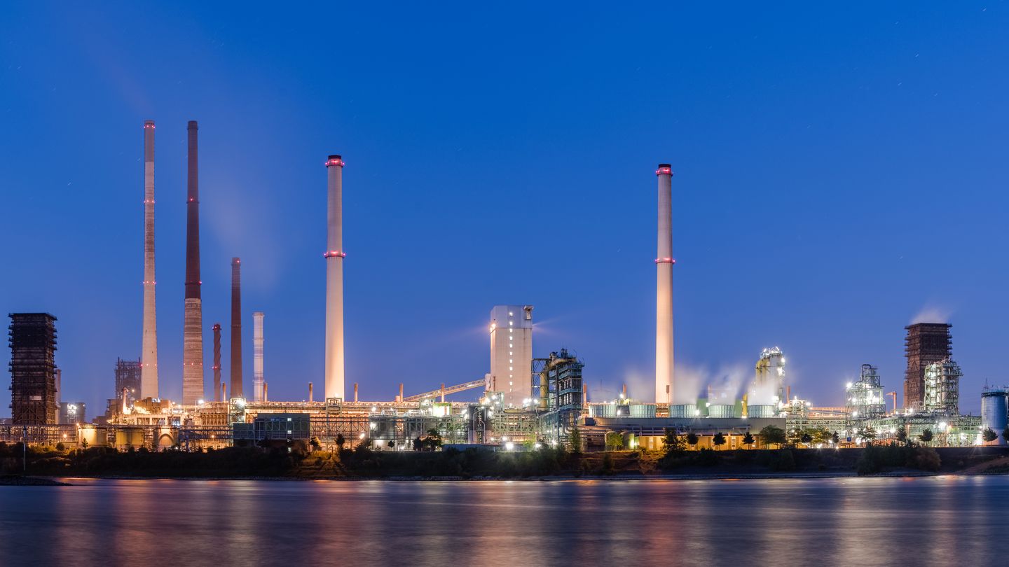 Industrieanlage mit Schornsteinen am Wasser in der Abenddämmerung